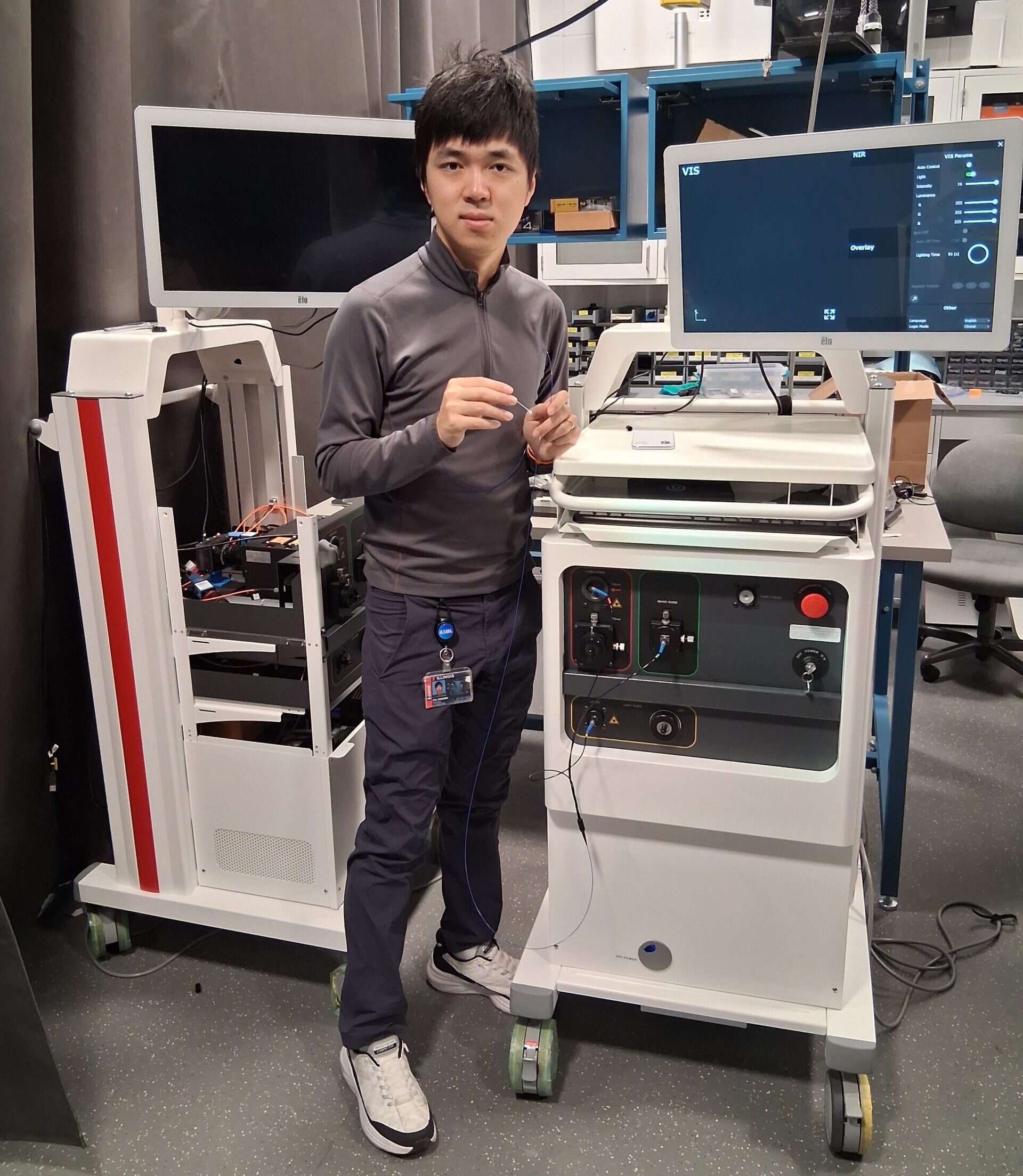 <em>For this project, doctoral student Zhongmin Zhu, shown here between two Johnson &amp;amp; Johnson Monarch&amp;trade; systems with the bronchial scope in hand, leads optical/electronic integration, camera firmware/ISP, and the mechanical redesign to fit the team&amp;rsquo;s imaging module inside the Monarch&amp;trade; system.<br></em><em>&amp;ldquo;What I love is that the tech collapses a complex optical train into one clean, stable module while boosting sensitivity and alignment robustness&amp;mdash;engineering elegance actually translating to clinical impact,&amp;rdquo; said Zhu.</em>