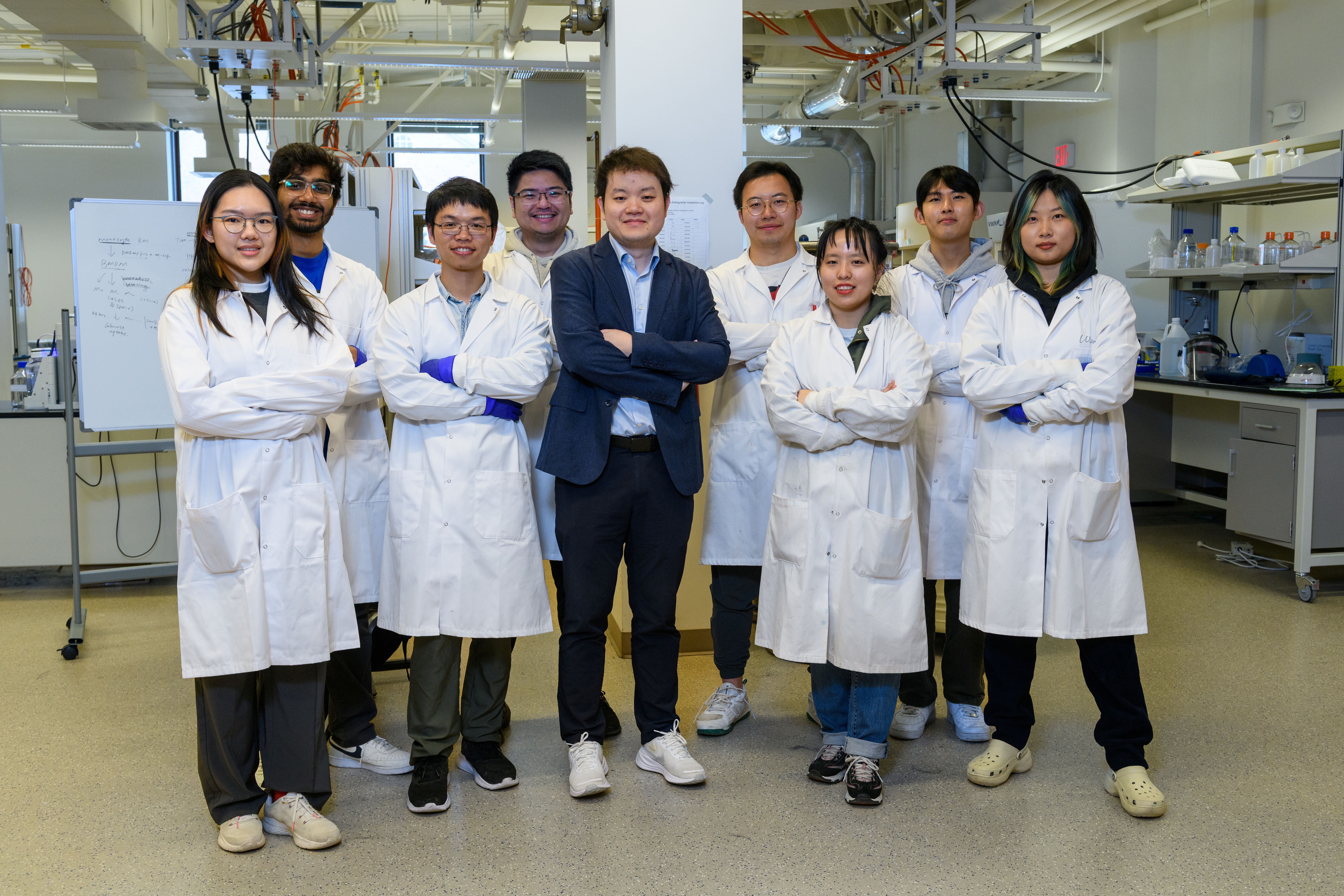 A group of people in lab coats stand looking at the camera with their arms crossed.