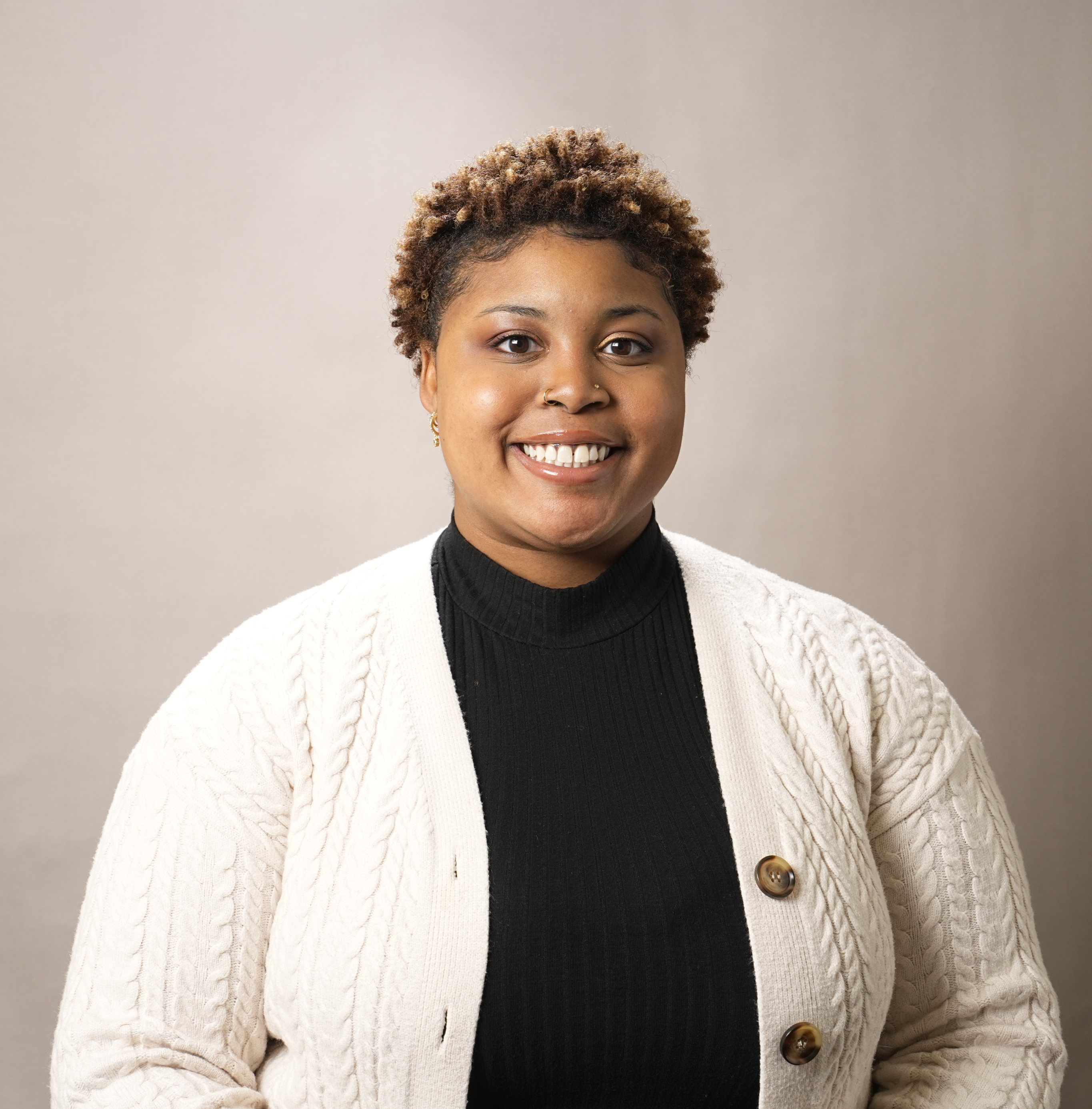 A student smiles at the camera in front of a brown background.