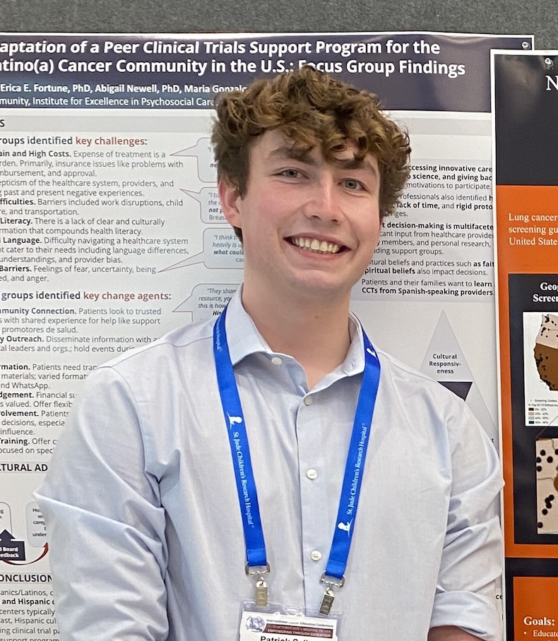 A student stands in front of a poster and smiles