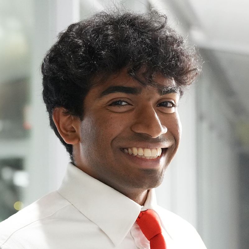A well dressed student with a red tie smiles at the camera