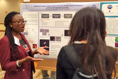 woman explaining research in front of research poster