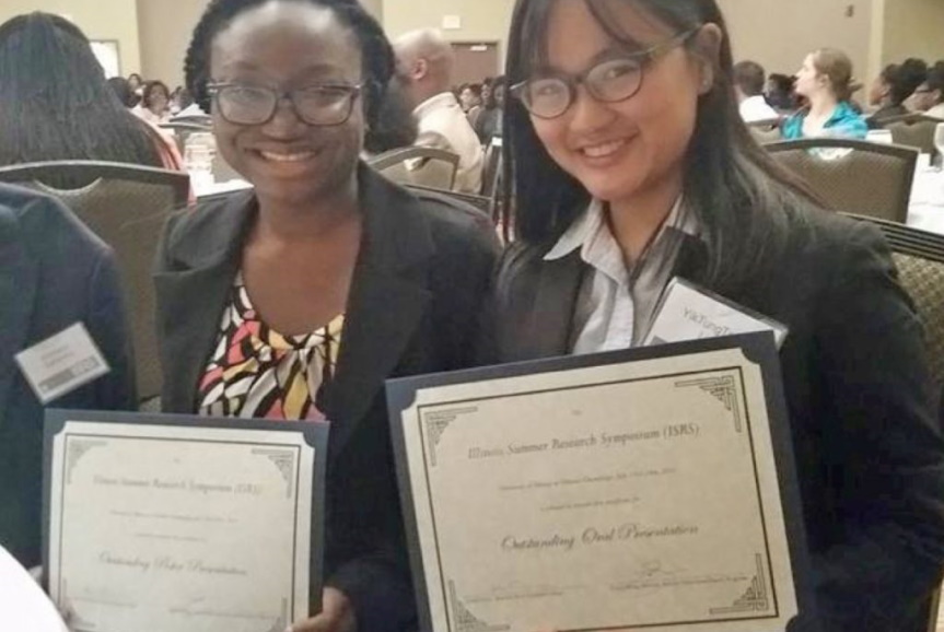 Two women hold certificates of achievement